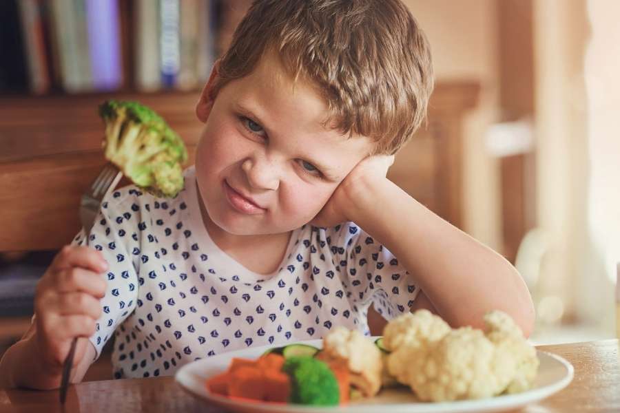 Un jeune garçon peu enthousiaste devant des légumes pour des repas équilibrés.
