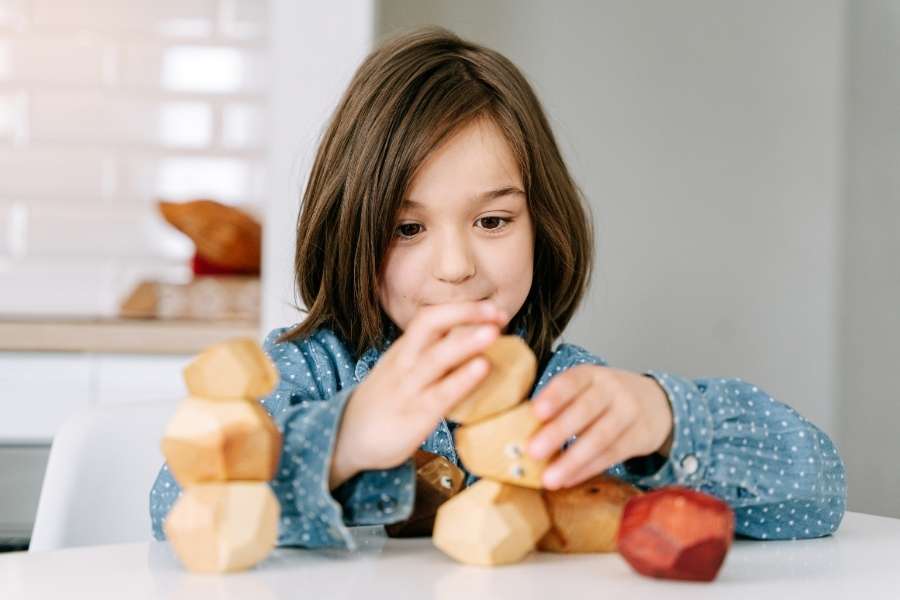 Jeune enfant concentré empilant des blocs de bois en forme de pierres, une activité Montessori.