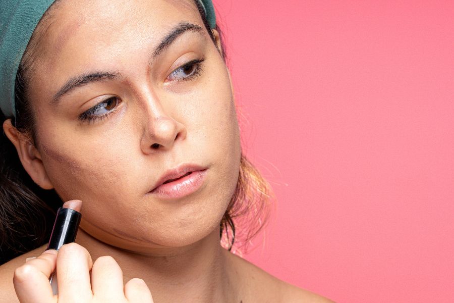 Une femme trace des lignes de contouring sur ses joues et son front avec un stick de maquillage.
